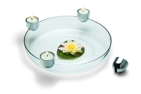 Glasschale mit einer schwebenden Lotusblume und drei brennenden Teelichtern in Haltern am Rand.