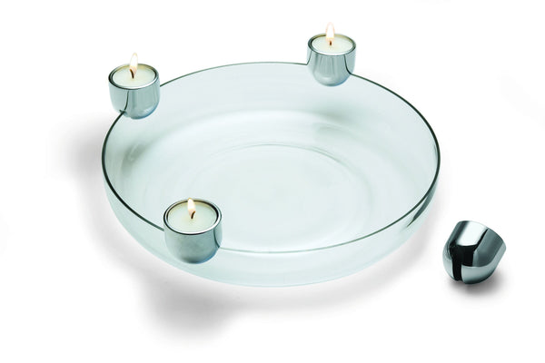 Eine runde Glasschale mit drei brennenden Teelichtkerzen in Metallhaltern und einem leeren Halter an der Seite.
