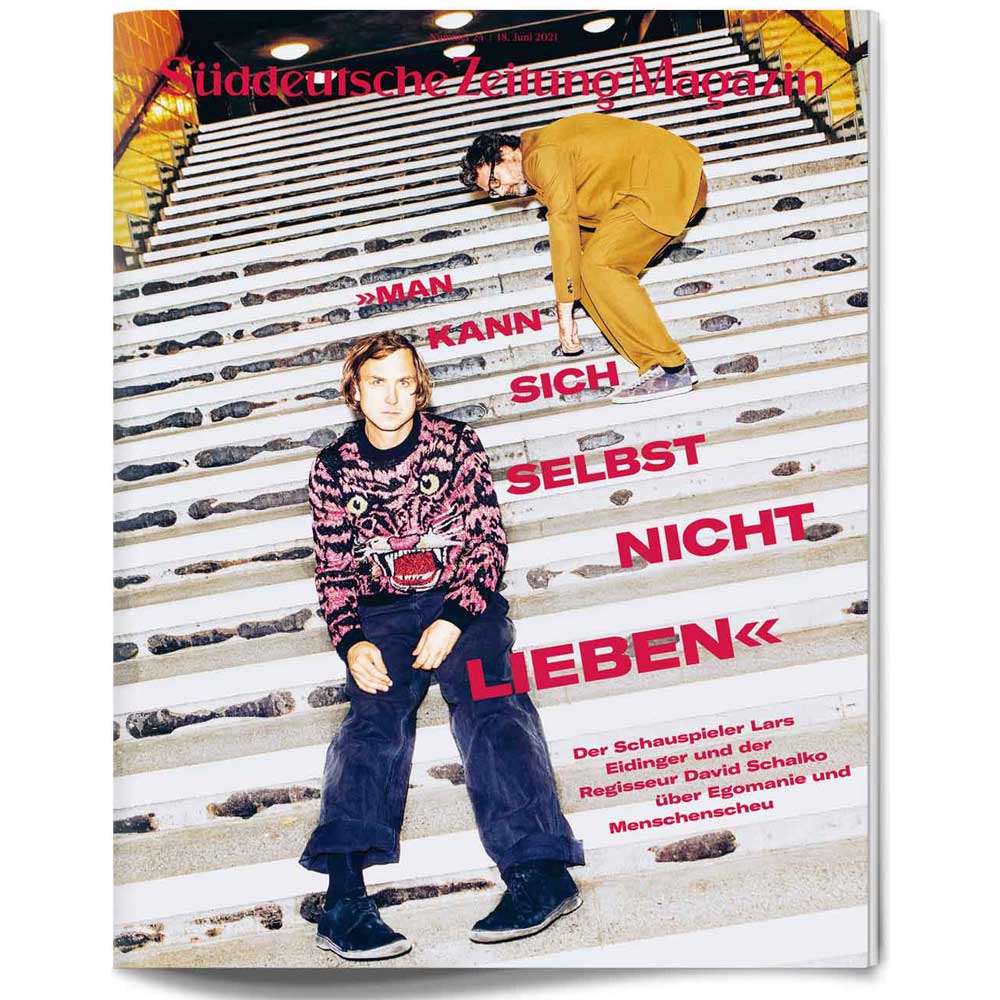 Zwei Männer posieren auf einer Treppe unter hellen Lichtern; ein fetter deutscher Text ist über das Bild gelegt.