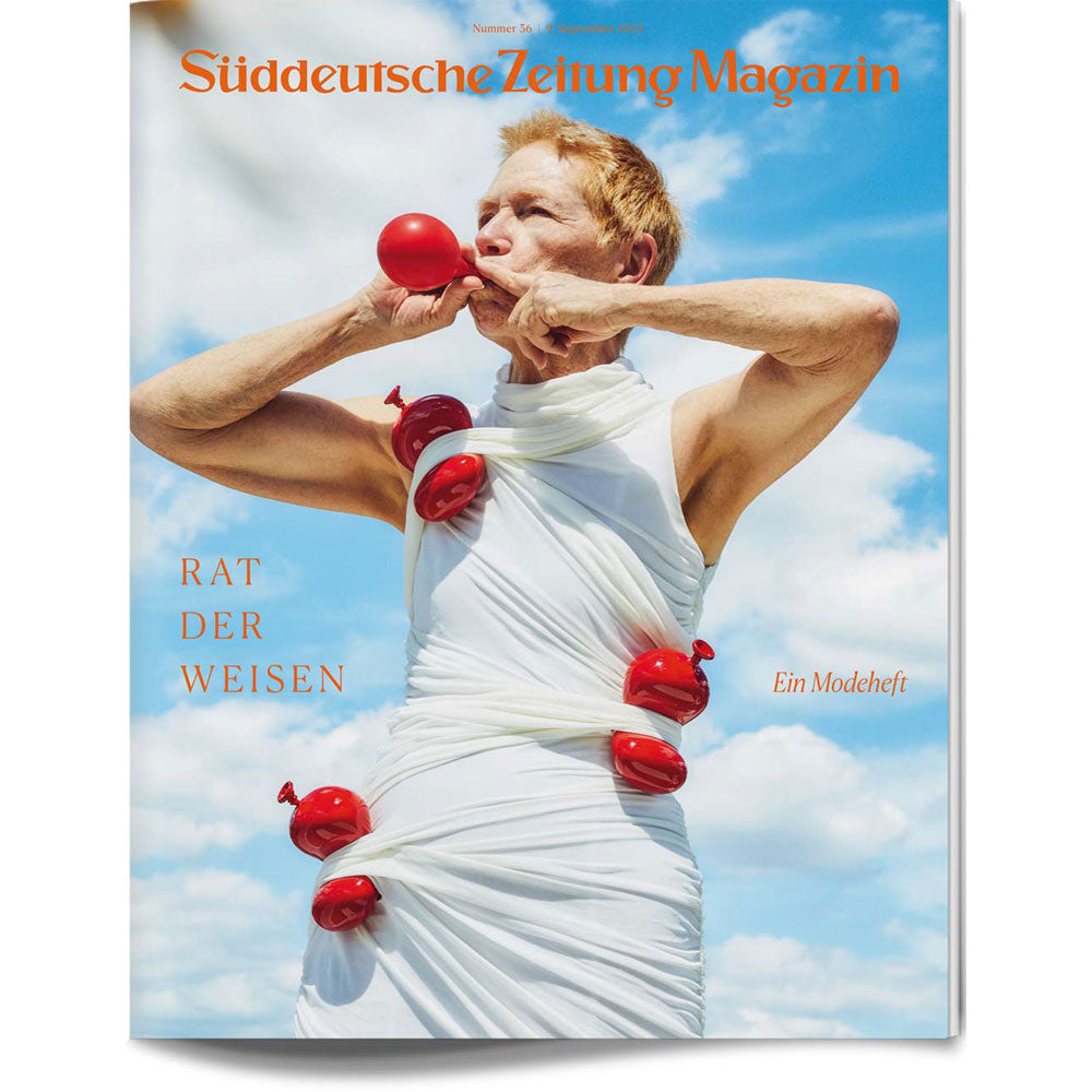 Eine weiß gekleidete Person steht vor dem Himmel und hat rote Luftballons in ihre Kleidung gesteckt.
