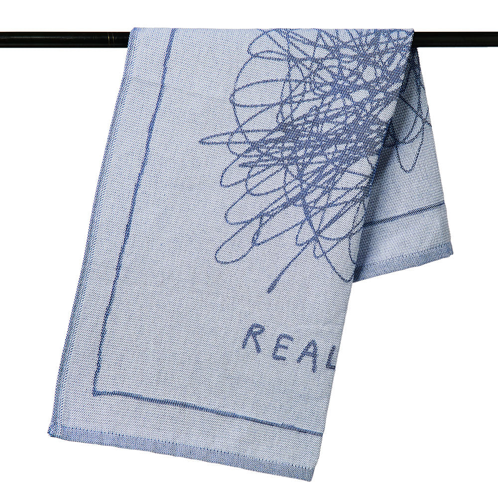 Hellblaues Handtuch mit dunkelblauer abstrakter Strichzeichnung und teilweisem Text mit der Aufschrift „REAL“, über eine Stange drapiert.