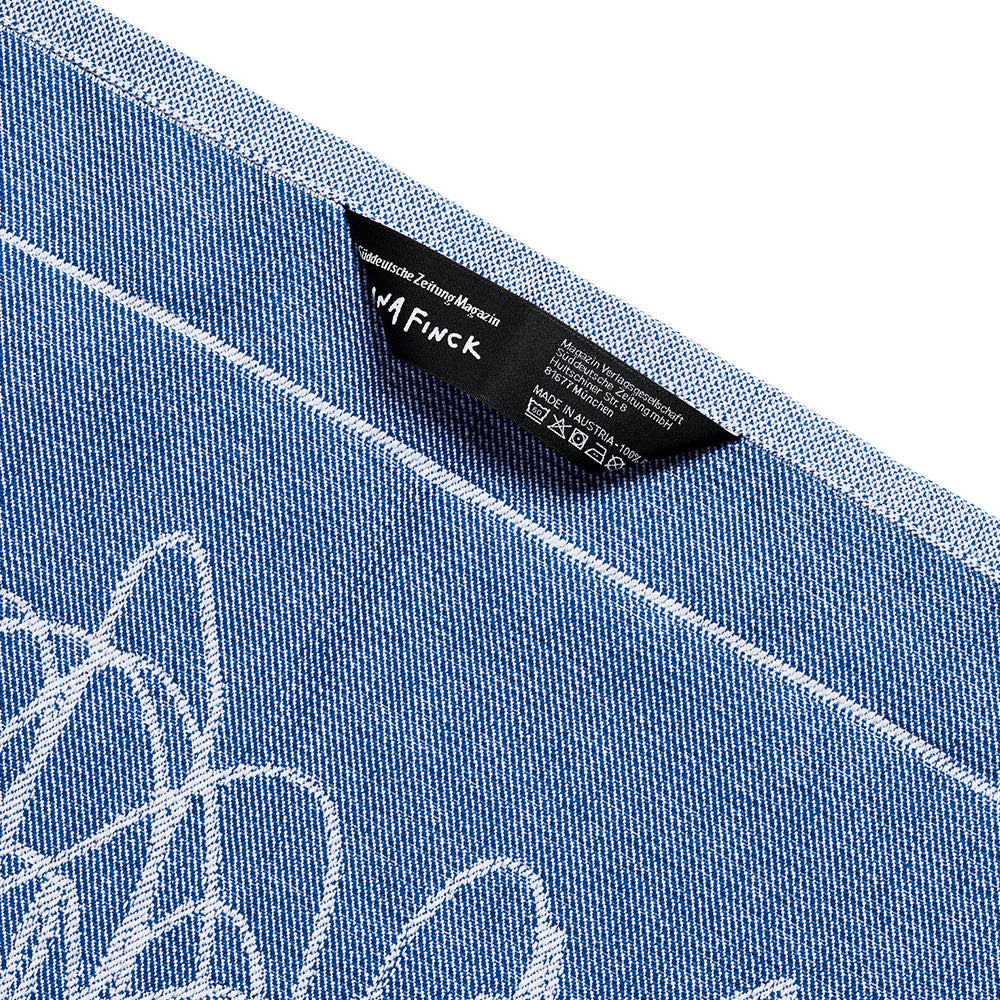 Nahaufnahme eines blauen Jeansstoffs mit weißen Nähten und einem in eine Naht eingenähten schwarzen Kleidungsetikett.