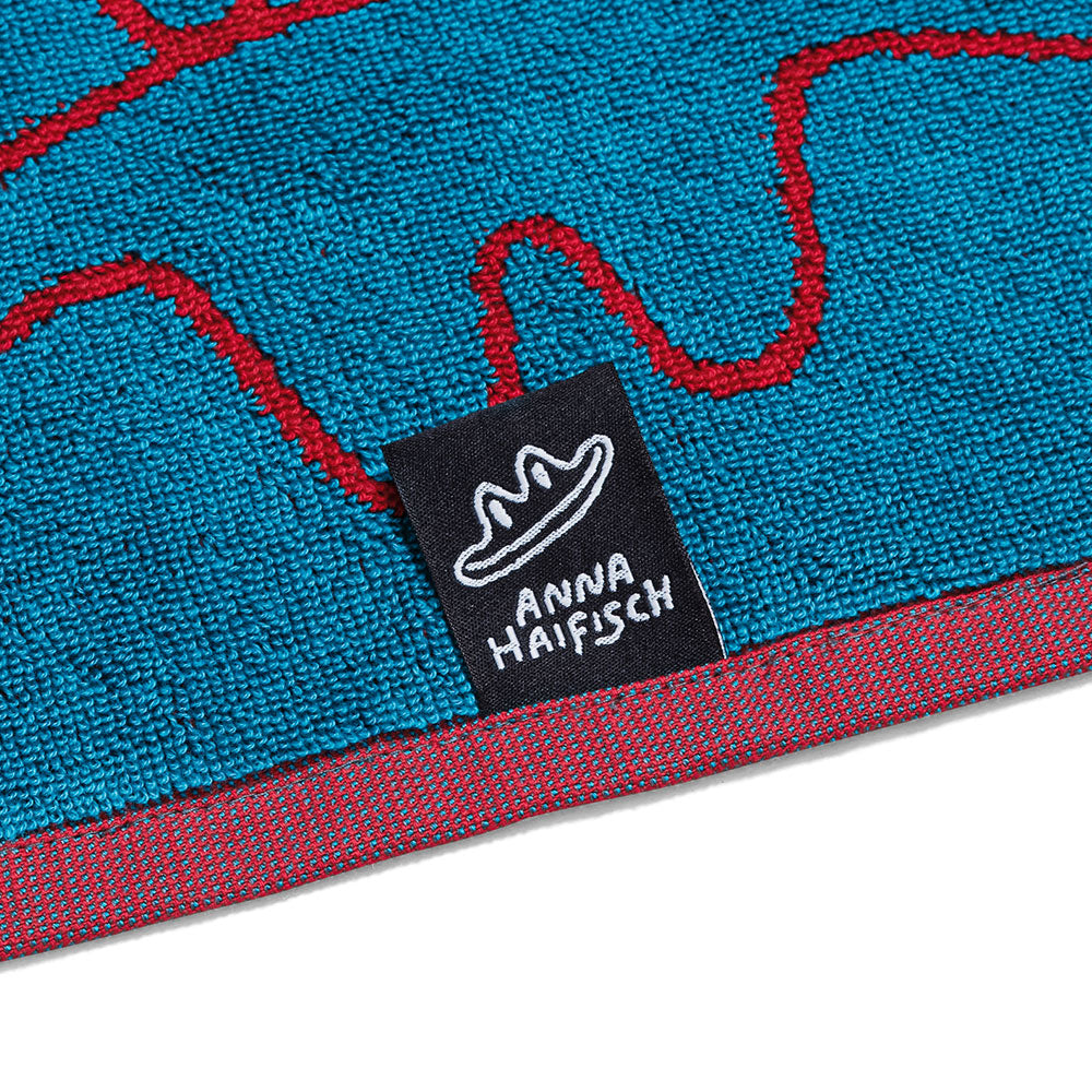 Nahaufnahme eines blauen Handtuchs mit roten Linien und einem schwarzen Etikett mit der Aufschrift „Anna Haifisch“ und einer Hutillustration.