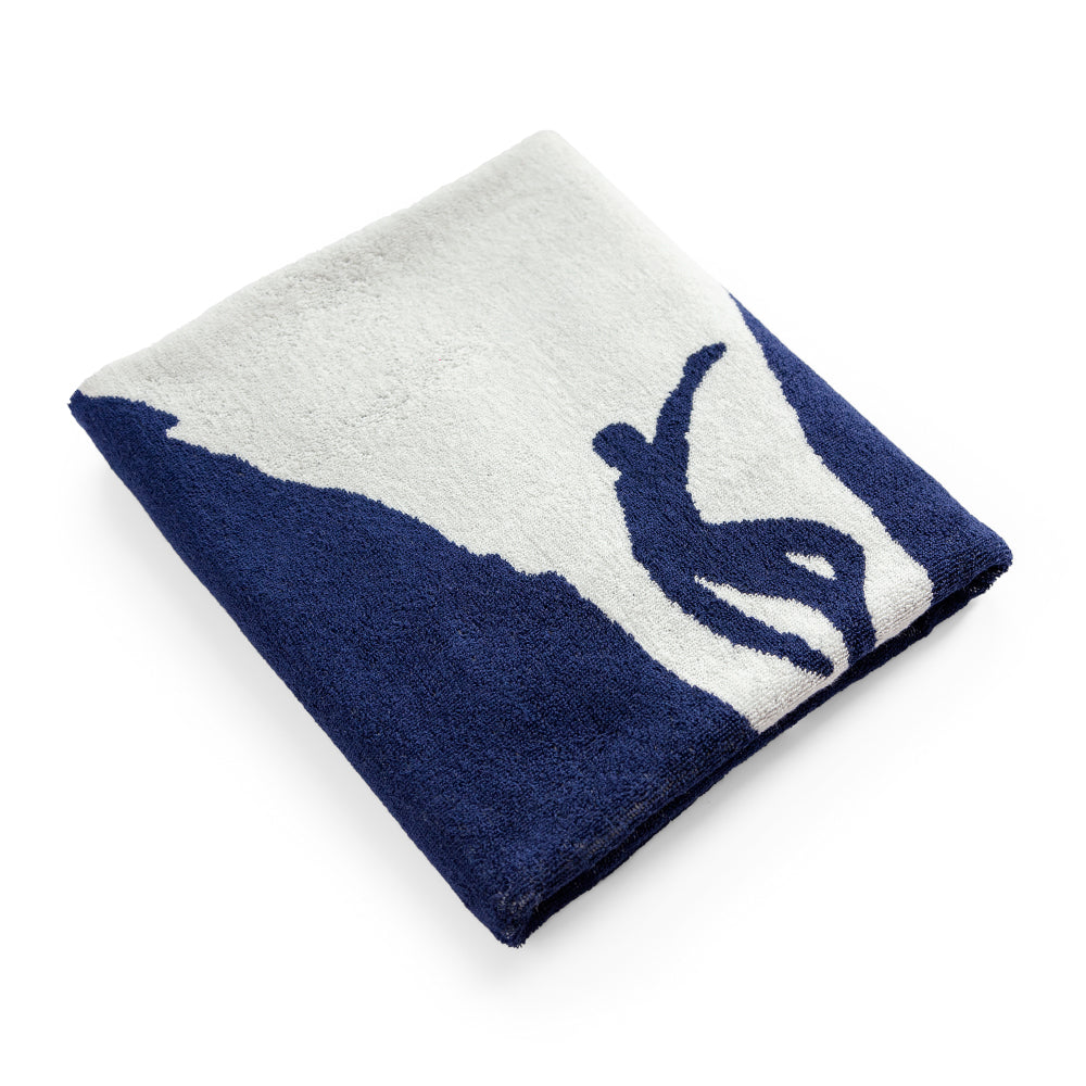 Gefaltetes Handtuch mit marineblauem und weißem Design, das die Silhouette eines Surfers zeigt, der auf einer Welle reitet.