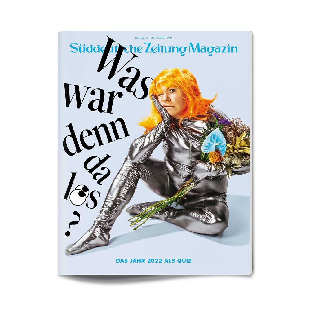 Person in silberglänzendem Outfit und orangefarbener Perücke mit Blumen in der Hand, die auf der Titelseite einer deutschen Zeitschrift sitzt.