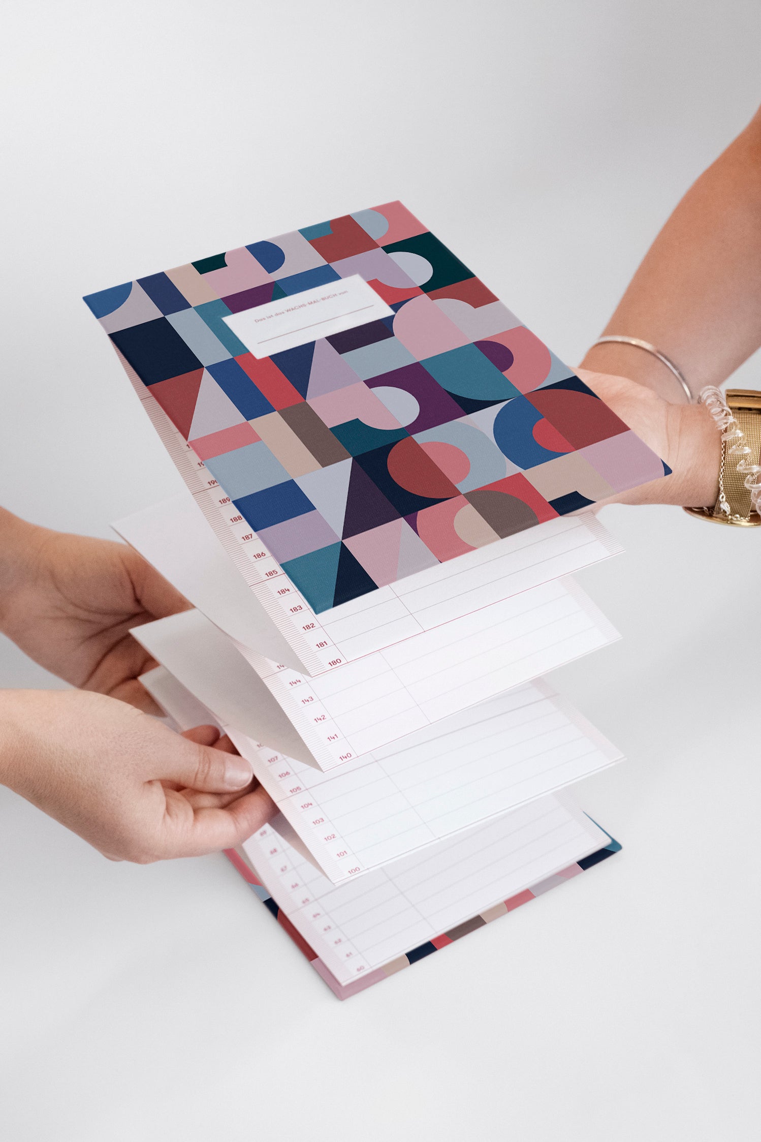 Zwei Personen halten einen bunten, geometrischen Wochenplaner in der Hand, dessen Seiten aufgeschlagen sind.