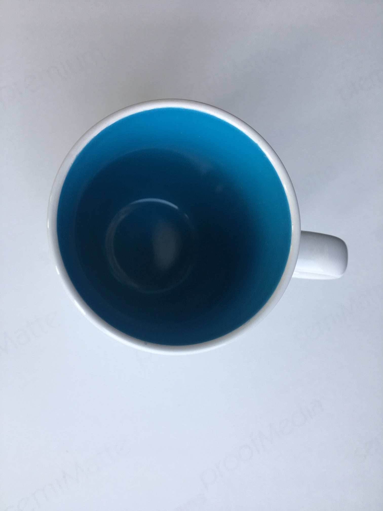 Weiße Keramiktasse mit blauer Innenseite, von oben auf einer weißen Oberfläche betrachtet.