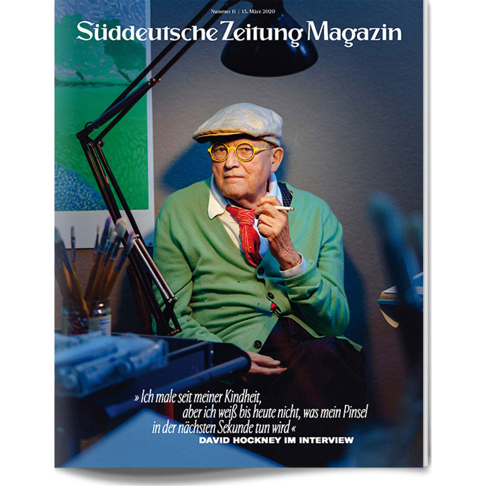 Ein älterer Mann mit Mütze und Brille sitzt in einem Kunstatelier und ist auf dem Cover einer Zeitschrift abgebildet.