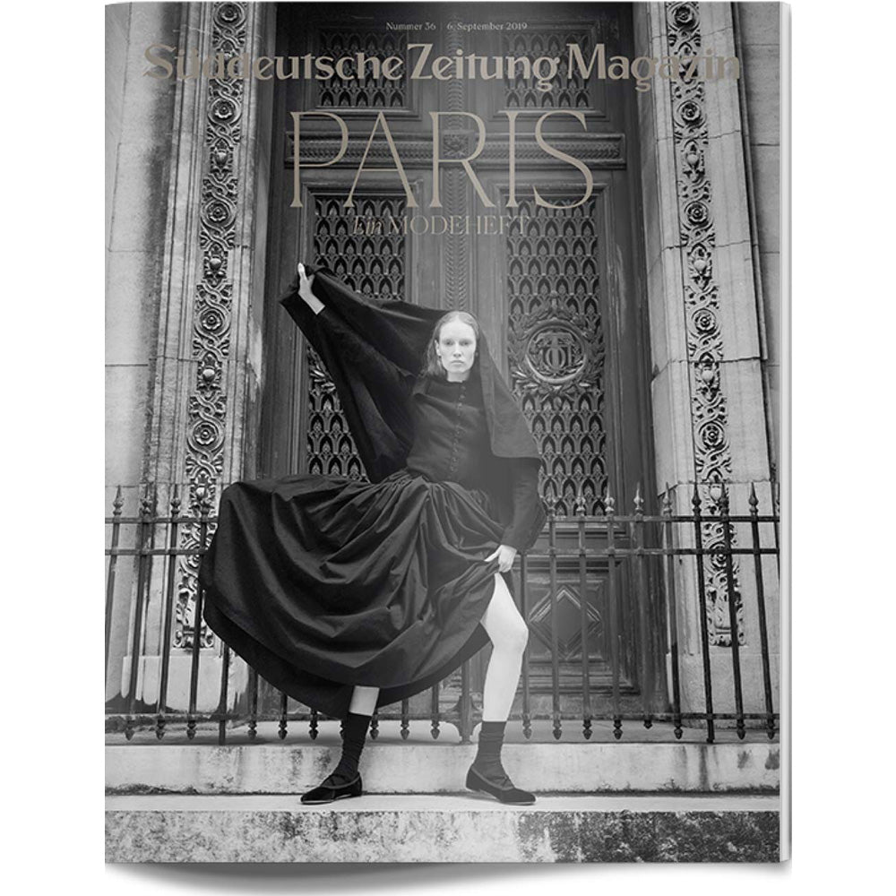 Eine Frau posiert in einem dramatischen schwarzen Outfit vor verschnörkelten Türen auf dem Titelbild einer Zeitschrift mit dem Titel PARIS.