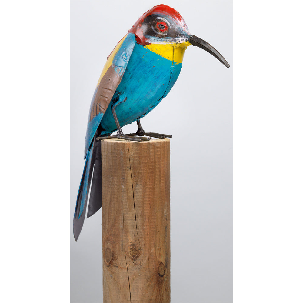 Eine farbenfrohe Vogelskulptur aus Metall, die auf einem Holzpfosten vor einem schlichten Hintergrund thront.