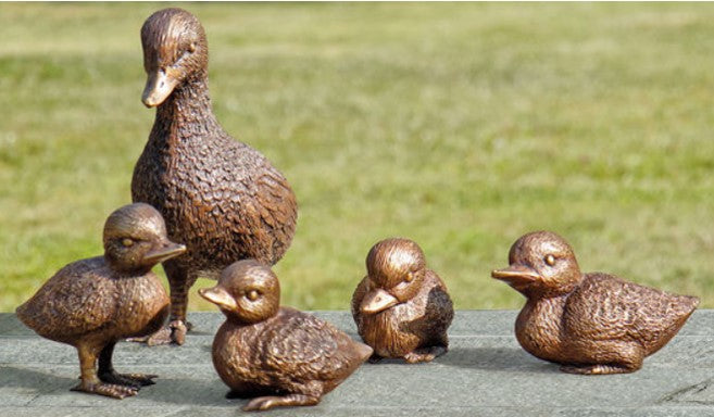 Bronzestatuen einer Ente und vier Entenküken auf einer Steinoberfläche mit Gras im Hintergrund.