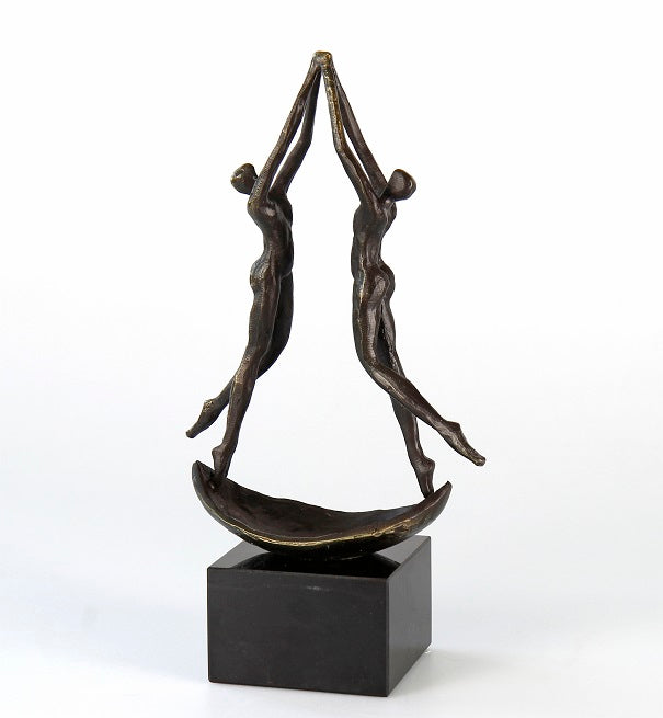 Bronzeskulptur zweier abstrakter menschlicher Figuren, die auf einem geschwungenen Sockel balancieren und nach oben greifen, auf einem schwarzen Podest.