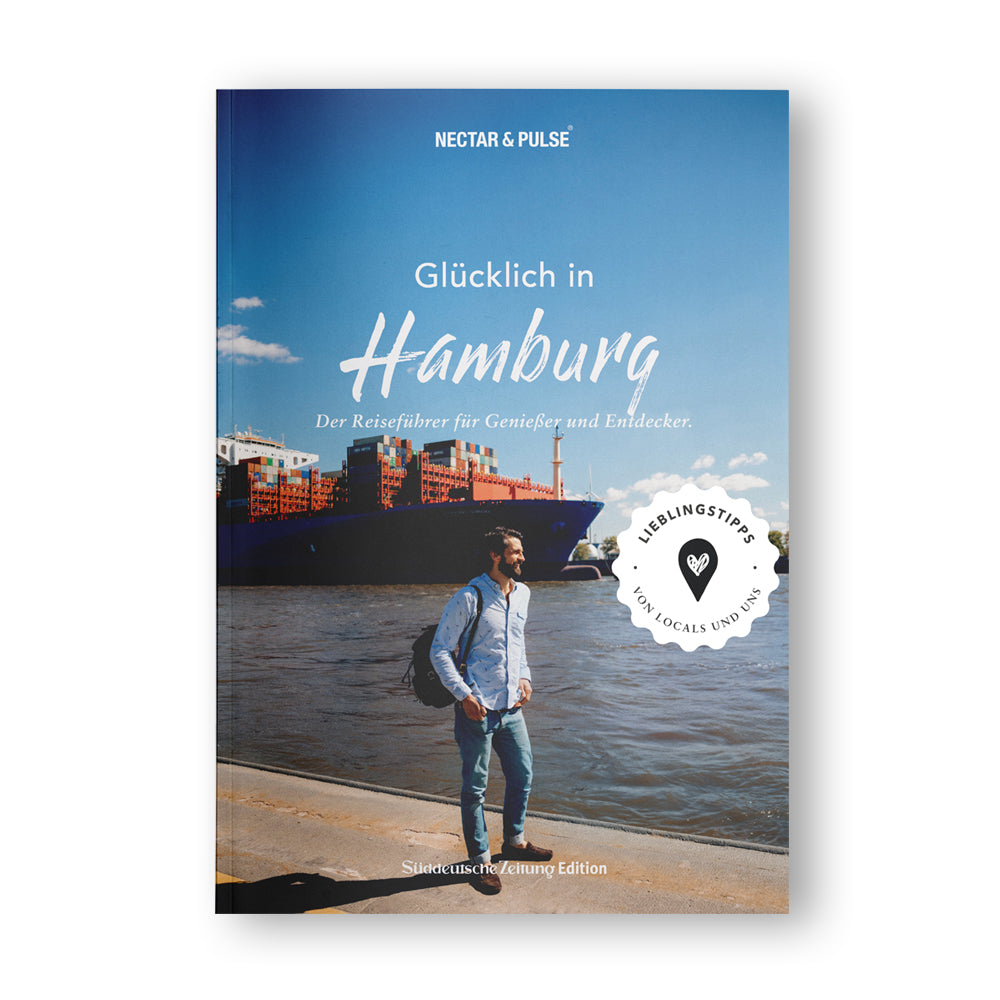 Ein Mann mit Rucksack steht am Hafen vor einem großen Schiff unter blauem Himmel; Buchcover „Glücklich in Hamburg“.