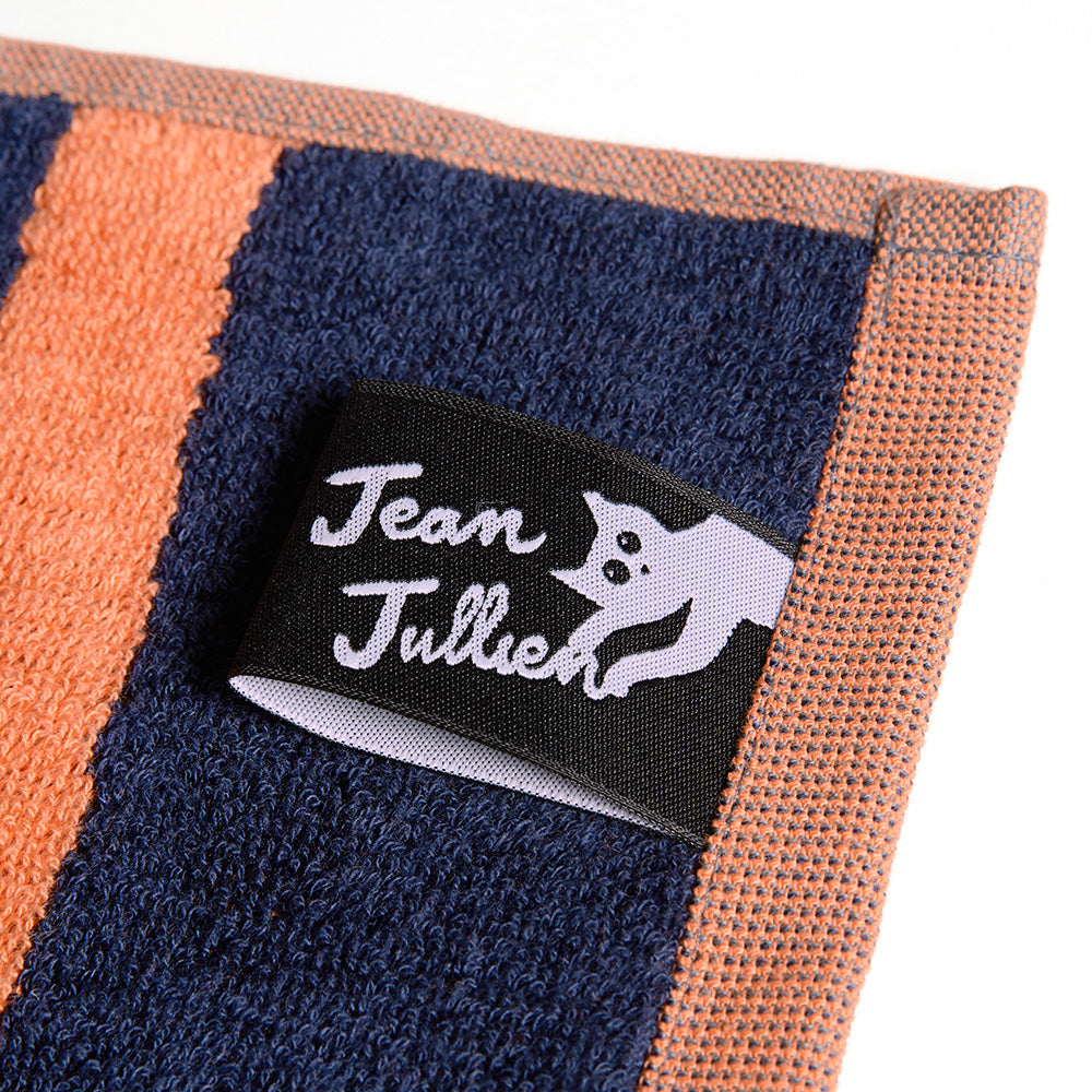 Ein marineblaues und orangefarbenes Handtuch mit einem schwarzen Jean Jullien-Etikett mit der Illustration einer weißen Katze.