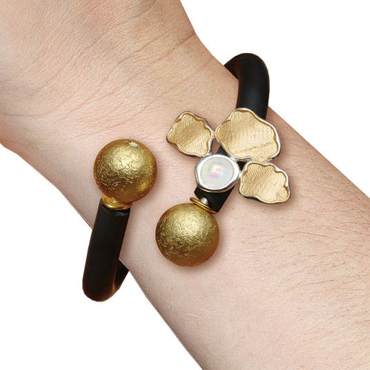 Ein schwarz-goldenes Armreif mit strukturierten Goldkugeln und blumenförmigen Akzenten am Handgelenk.