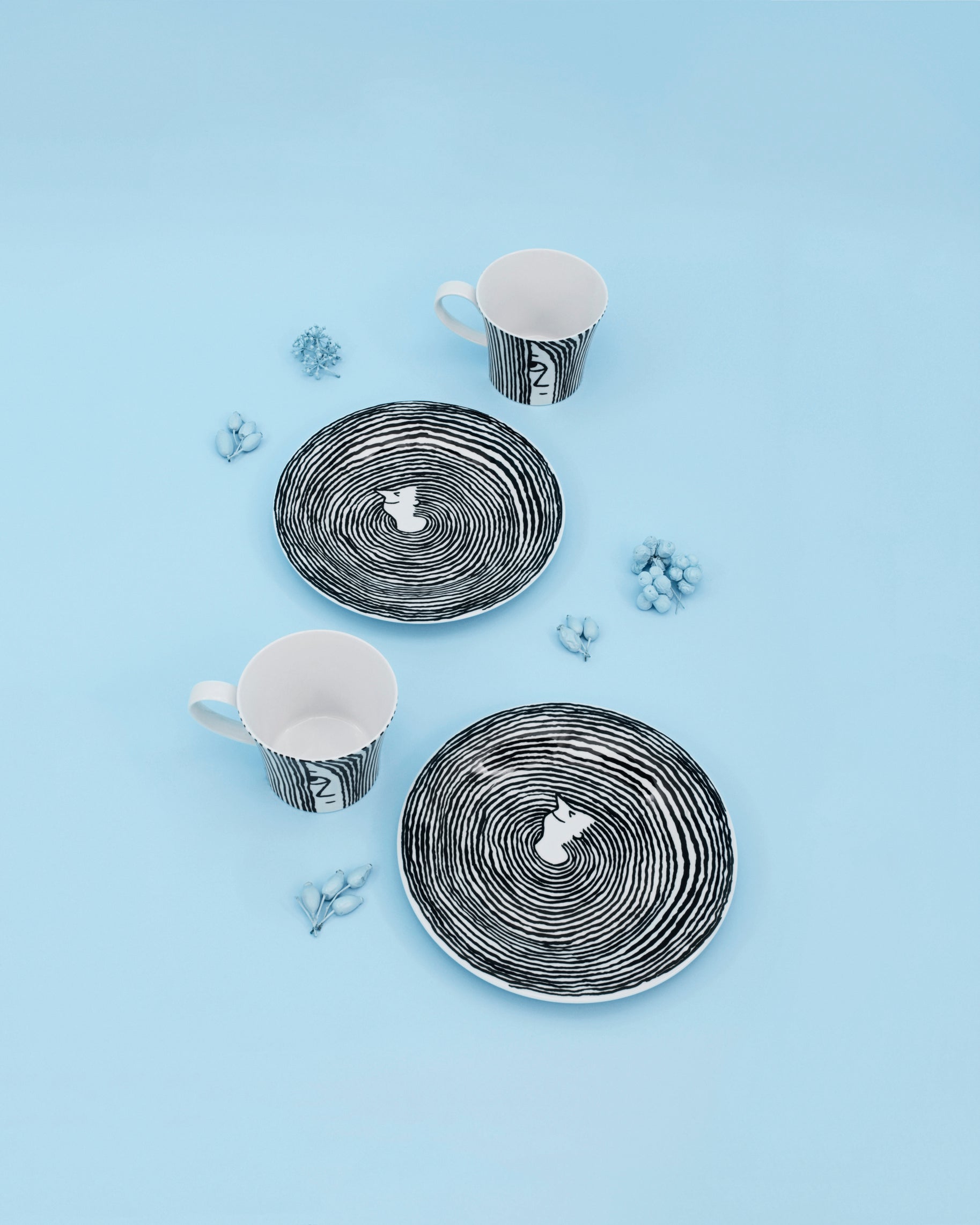 Die Porzellan-Frühstücks-Tasse „Bonjour BERLIN“ wird neben schwarz-weißen Tellern mit Katzenmotiven auf hellblauem Untergrund mit dekorativen blauen Beeren präsentiert.