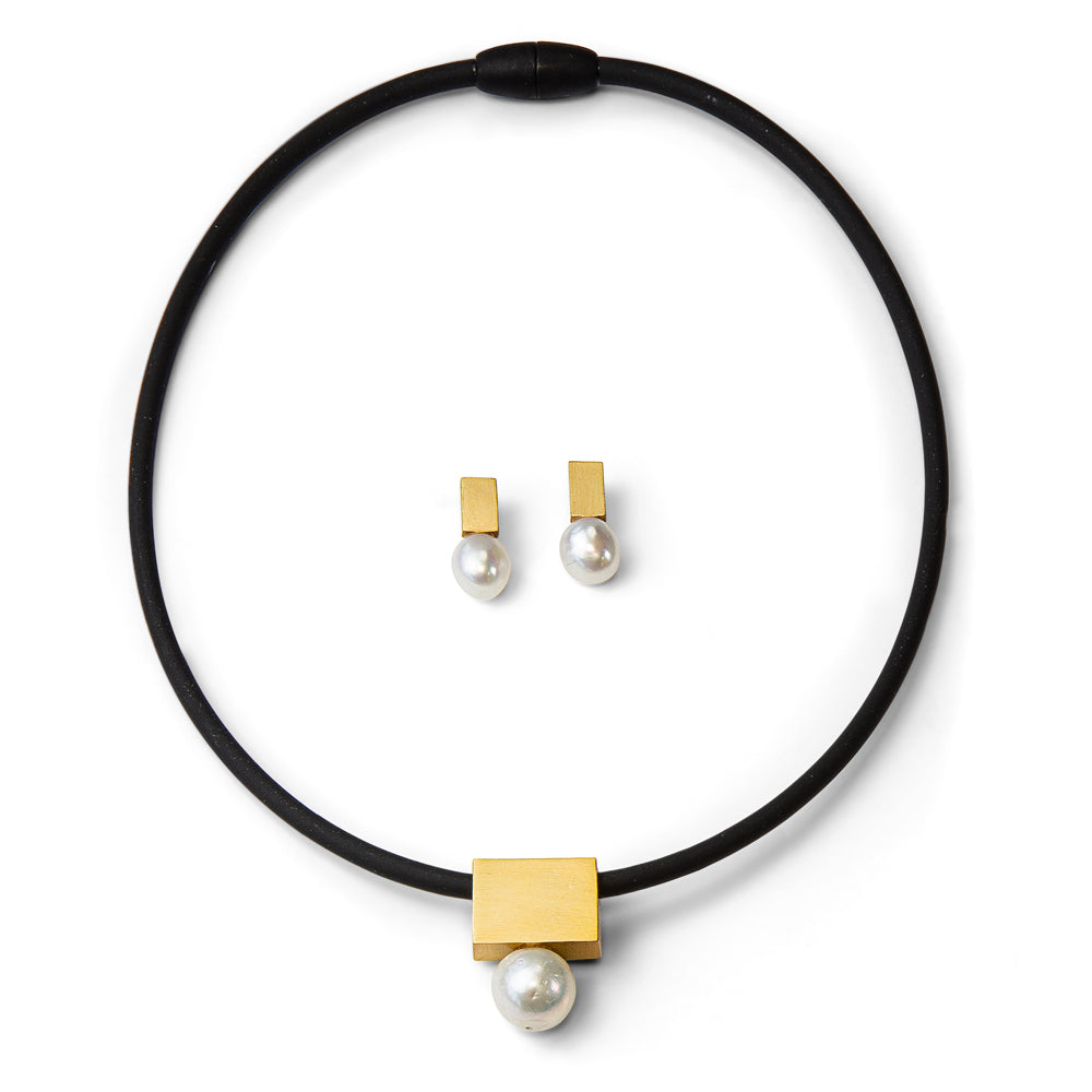 Schwarze Halskette mit goldenem Quadrat und Perle, passende Ohrstecker aus Gold und Perle auf weißem Hintergrund.
