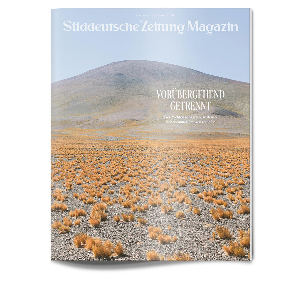 Magazinumschlag mit einer grasbewachsenen Ebene, spärlichen Sträuchern und einem großen Hügel unter klarem Himmel; deutscher Text überlagert.