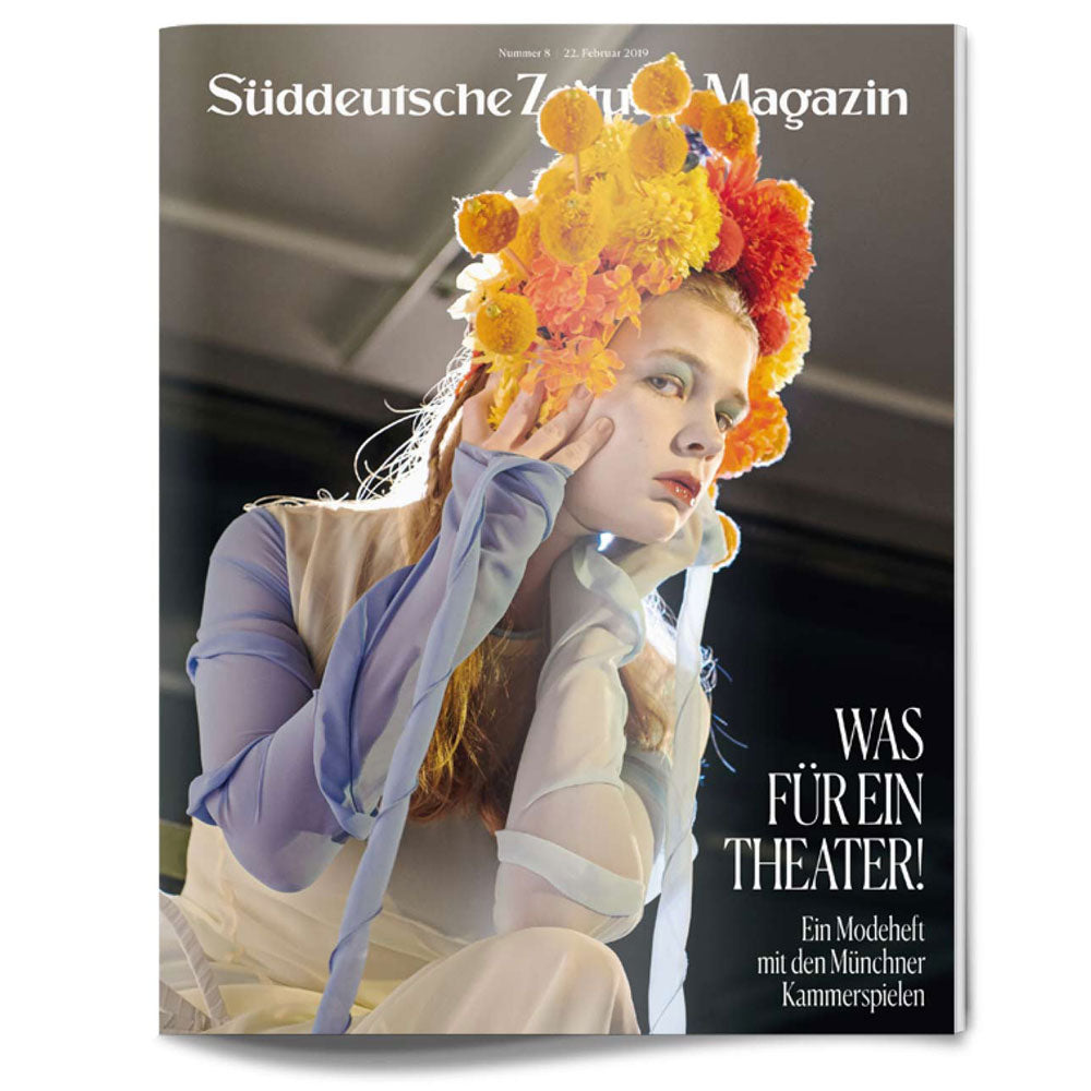 Eine Frau in einem durchsichtigen blauen Kleid und einer leuchtend gelben Blumenkrone posiert auf dem Cover einer Zeitschrift.