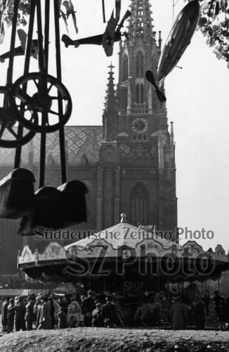 Oldtimer-Karussell und Menschenmenge vor einer großen gotischen Kirche mit einem hohen Uhrenturm im Hintergrund.