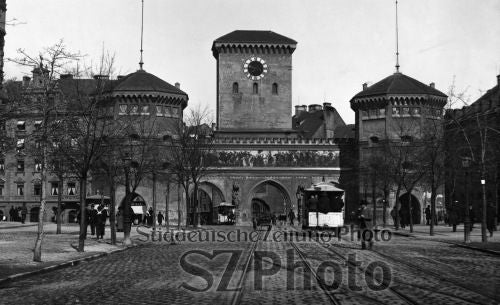 Historisches Schwarz-Weiß-Foto eines Stadttors mit drei Türmen und einer davor fahrenden Straßenbahn.