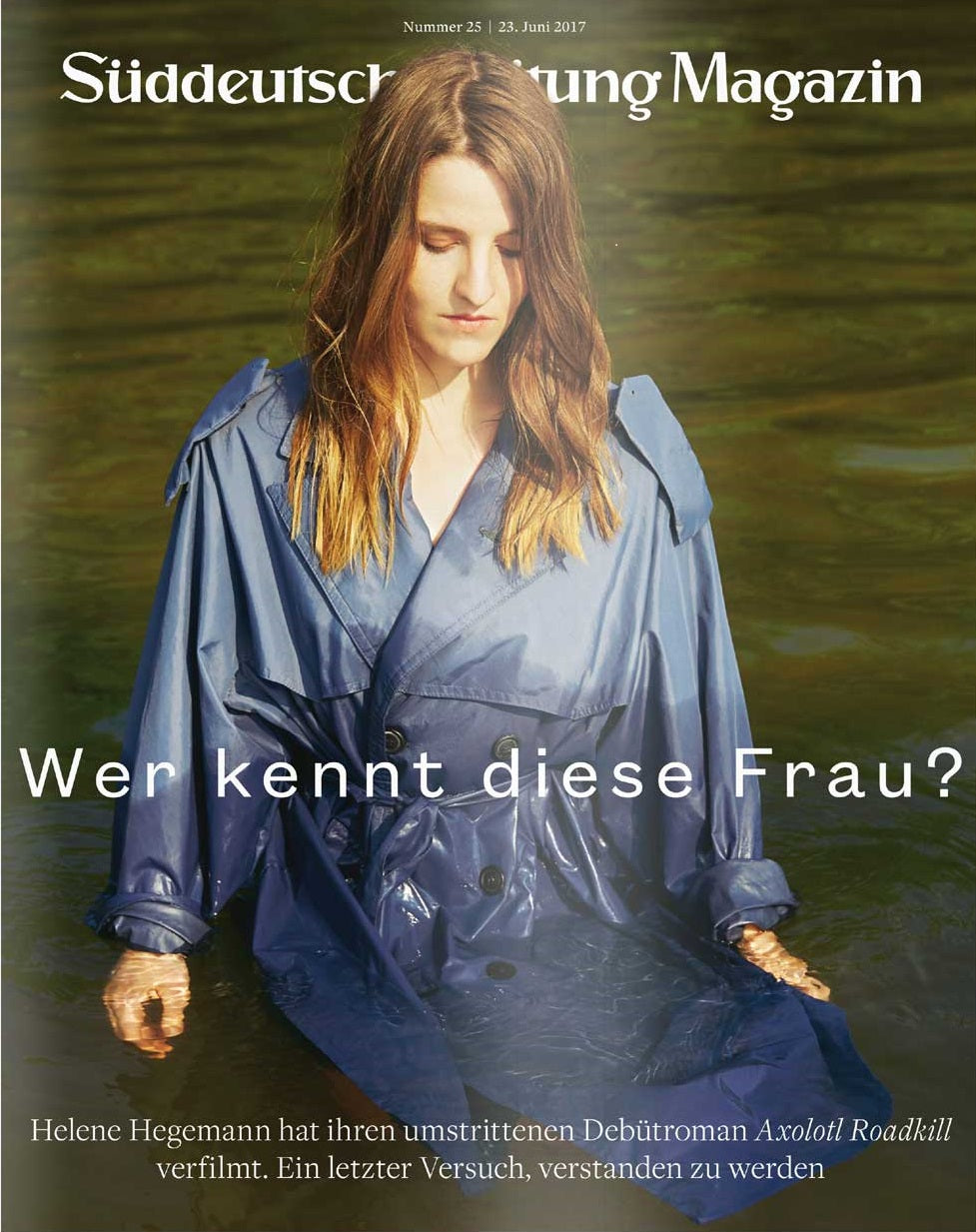 Eine Frau in einem blauen Regenmantel steht im seichten Wasser und blickt nach unten, wie auf dem Titelbild einer Zeitschrift.