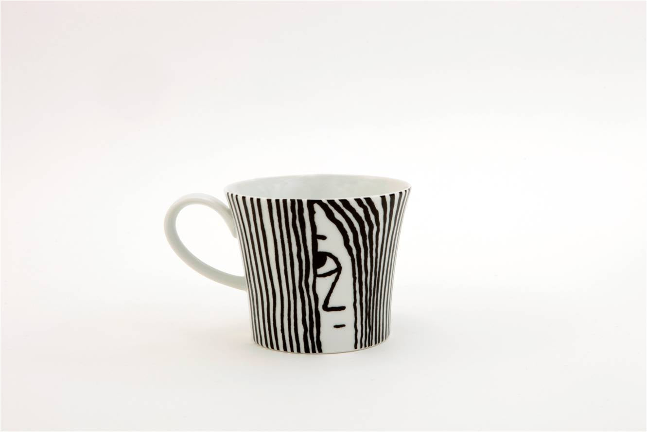 Porzellan Frühstücks-Tasse „Bonjour BERLIN“: Weiße Tasse mit vertikalen schwarzen Streifen, die auf einer Seite ein abstraktes Gesicht bilden, auf weißem Hintergrund.